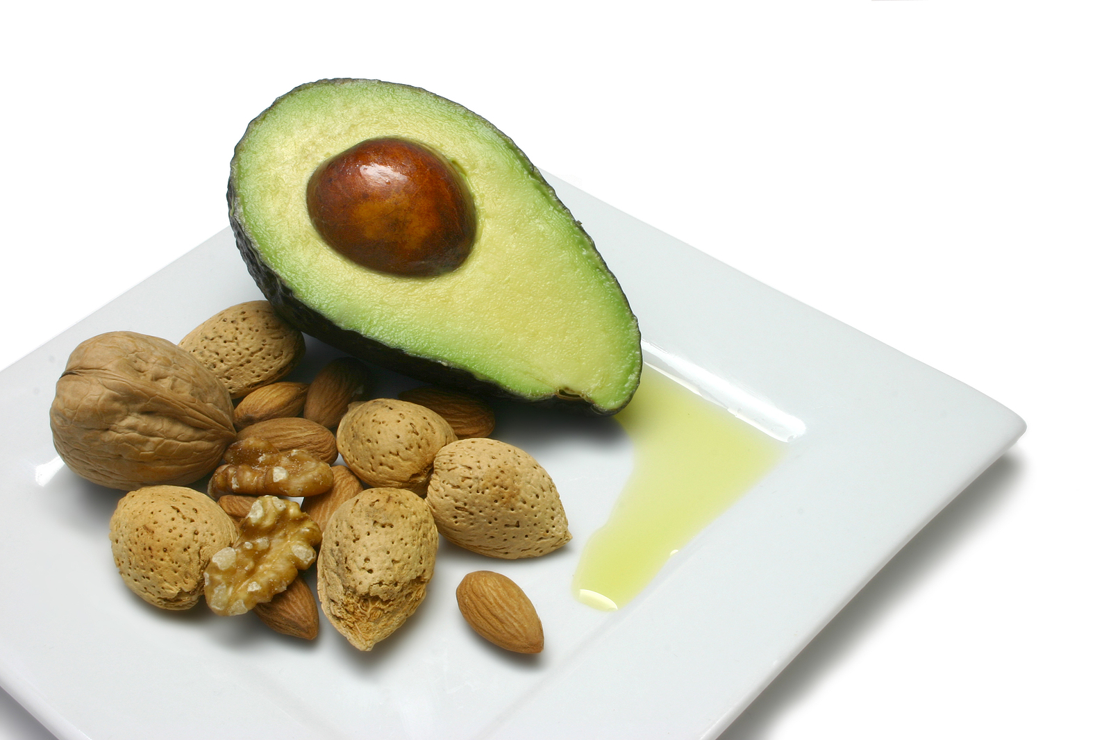Half an avocado with walnuts and almonds on a white plate