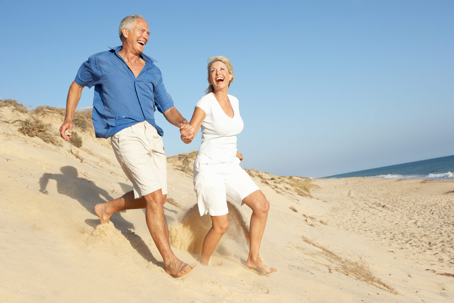 Older couple running down a sand dune holding hands